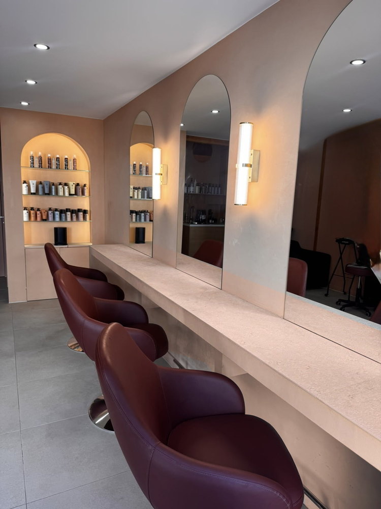 Le salon : fauteuils bordeaux alignés devant les miroirs en arche et la niche de soins rétroéclairée